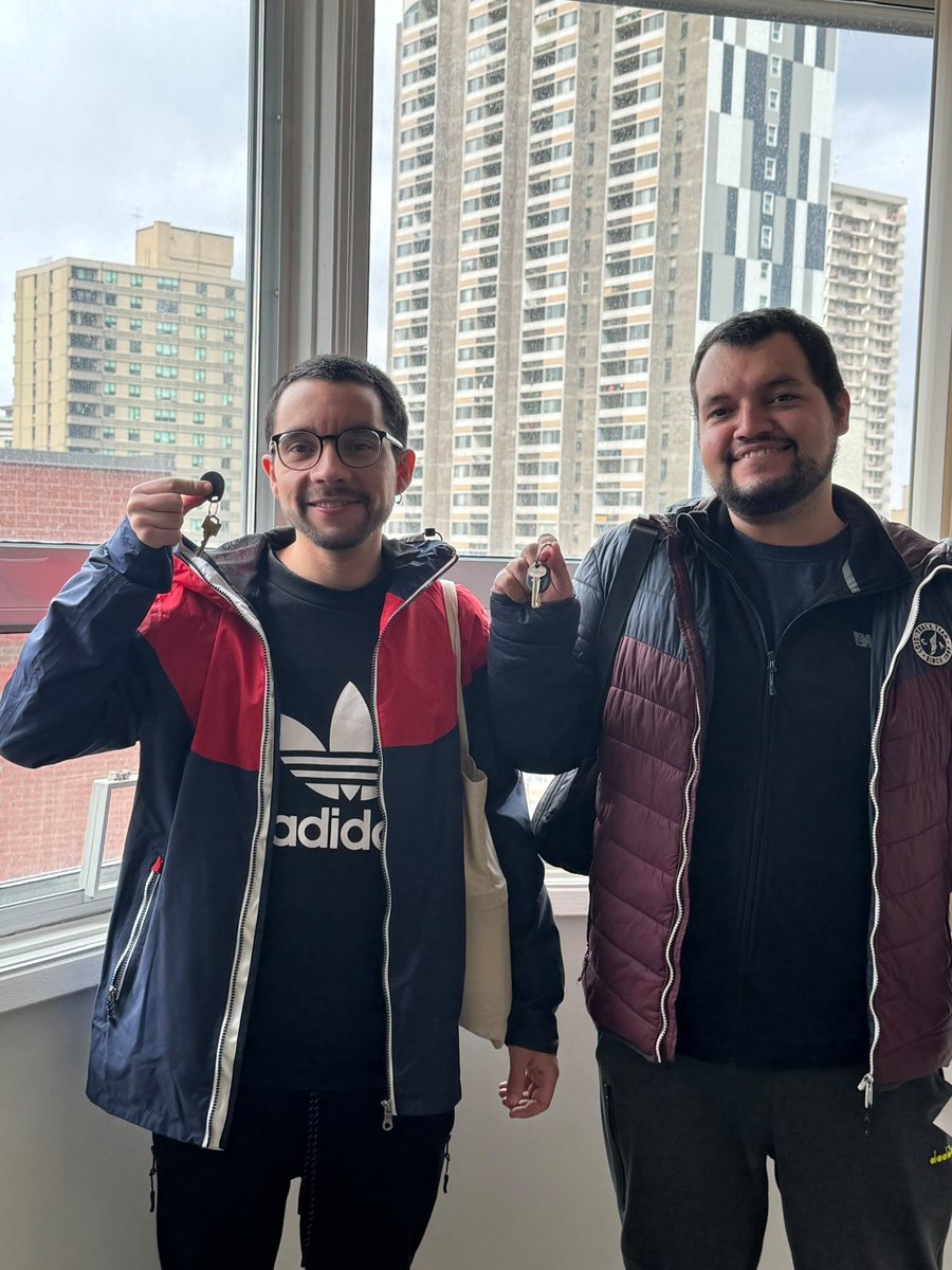 Dos clientes mostrando llaves frente a una ventana con vista urbana