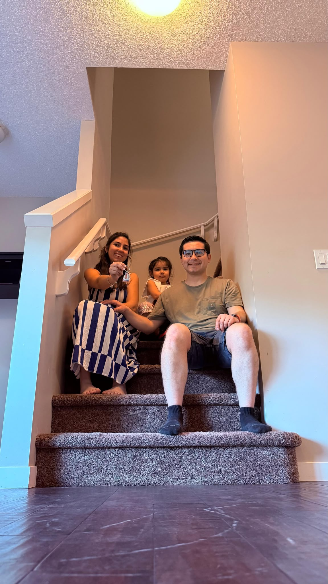 Familia de clientes sentada en las escaleras de su nuevo hogar con llaves